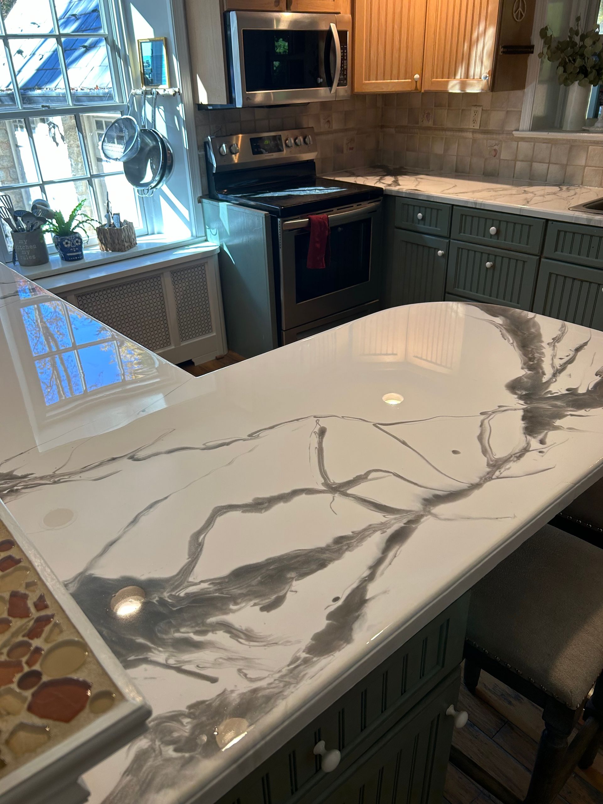 A kitchen island with a white and gray veined countertop, featuring a stove and cabinets in the background.