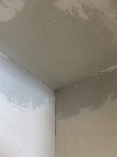 A worker in a yellow shirt and protective eyewear uses a long-reach power sander to smooth a white ceiling.