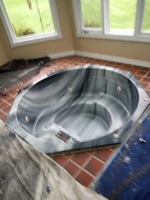 A deep, grey marbled jetted bathtub sits in a sunlit corner on a terracotta tiled floor.