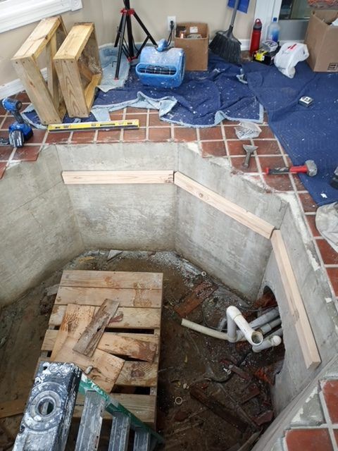 An indoor construction site features an excavated area with exposed concrete, wooden supports, and plumbing pipes.