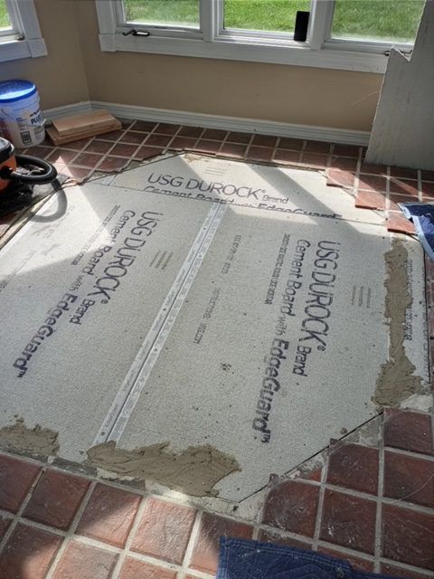 New sheets of USG Durock cement board installed on a floor with surrounding red quarry tiles, showing unfinished joints.