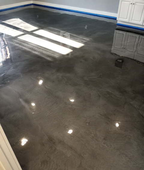 A high-gloss, metallic grey epoxy floor with swirling patterns and white cabinet trim in an indoor room.