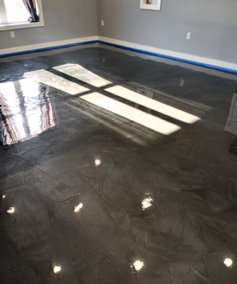 A gray, high-gloss metallic epoxy floor in a room, with sunlight reflecting onto the surface near a window.