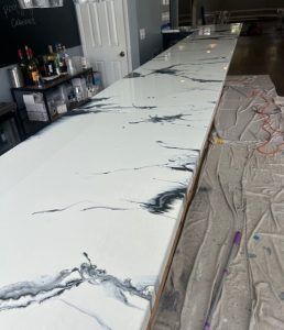 A white epoxy countertop with dark, marble-like veins, shown in a workshop setting with protective drop cloths on the floor.