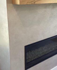 A modern fireplace with a linear black insert set into a smooth, light beige concrete-style wall below a wooden mantel.