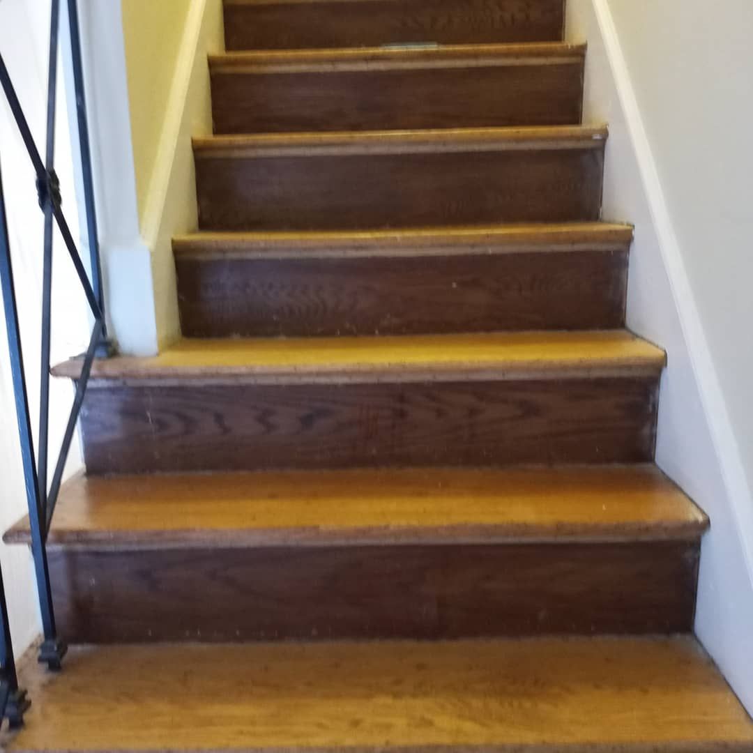 A view looking up a wooden staircase with dark brown treads and risers, flanked by a metal railing and white walls.