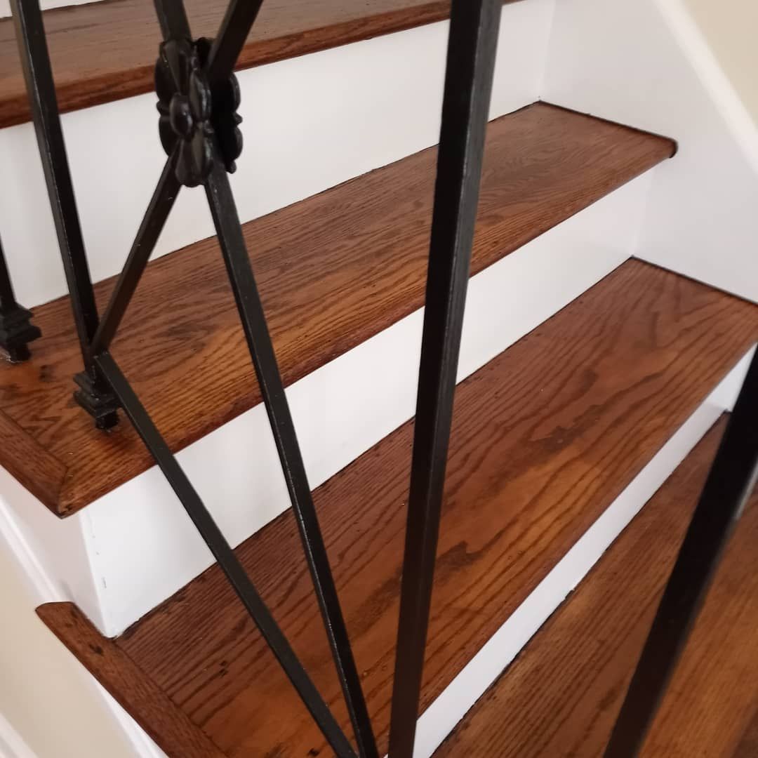 Wooden stair treads with white risers and a black wrought-iron railing with ornate scrollwork.