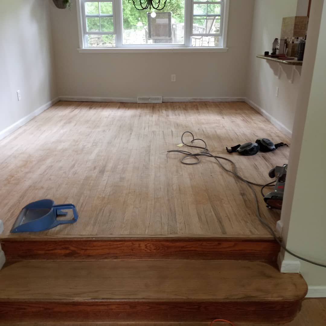 A room with a sanded, light-colored wooden floor, a step, and a window, showing home renovation in progress.