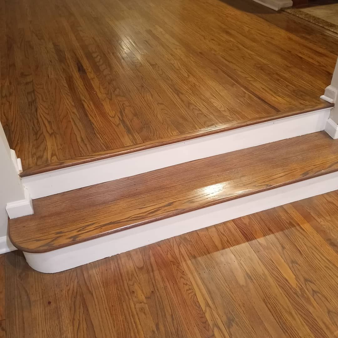 A single wooden stair step with a white riser, connecting a dark wood-floored upper level to a similar lower floor.