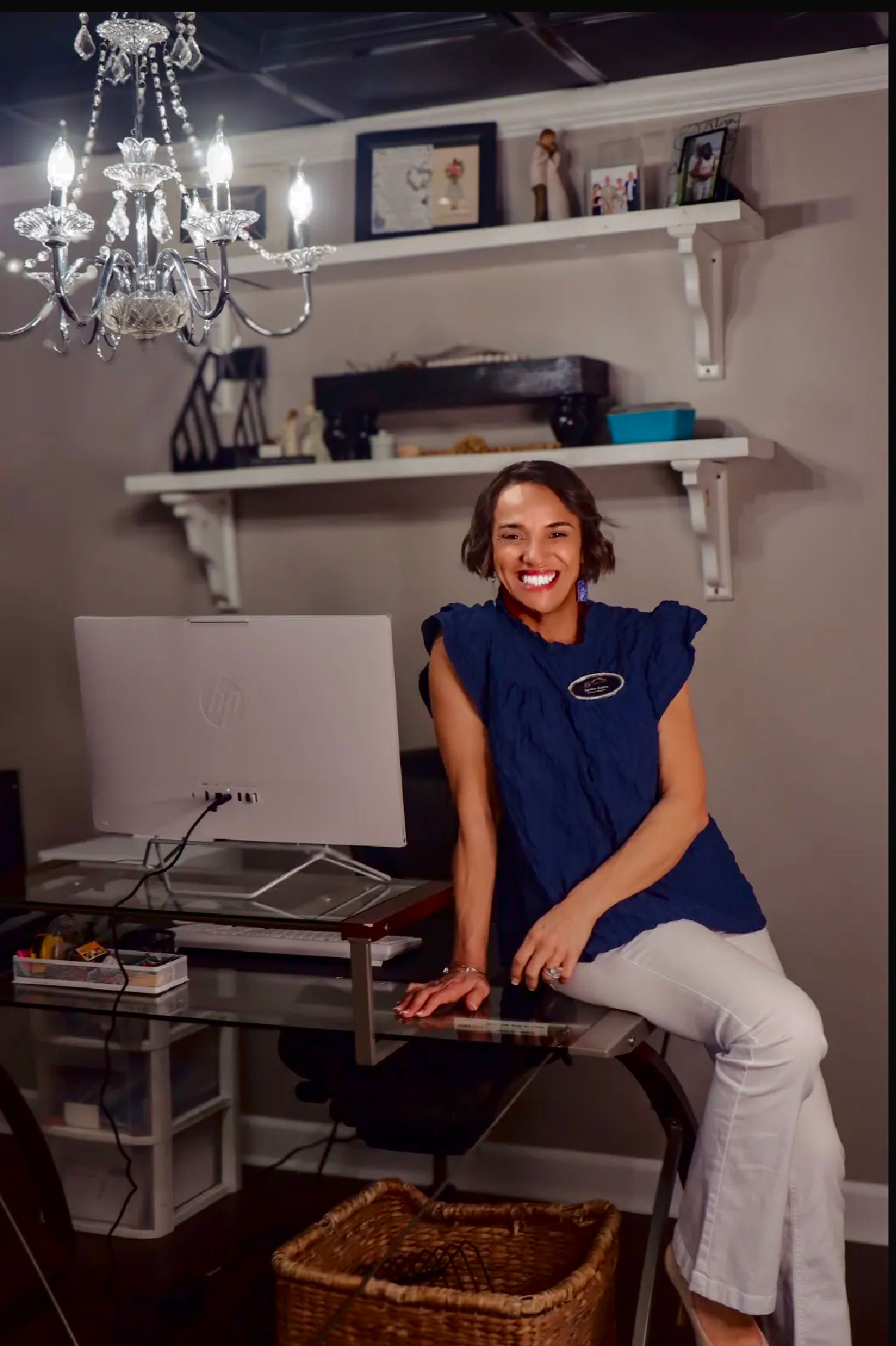 A woman is sitting at a desk with a laptop and a vase of flowers.