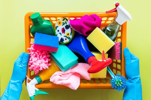 Gloved hands holding a box of colorful cleaning supplies and sponges on a yellow background
