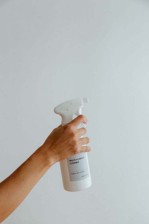 Hand holding a white spray bottle against a plain light background