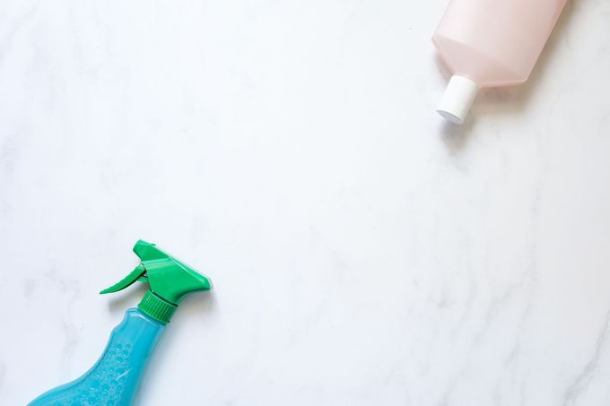 Two spray bottles on a light marble surface, one blue at bottom left and one pink at top right