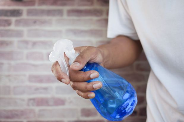 Hand spraying blue cleaner from a white trigger bottle against a brick wall
