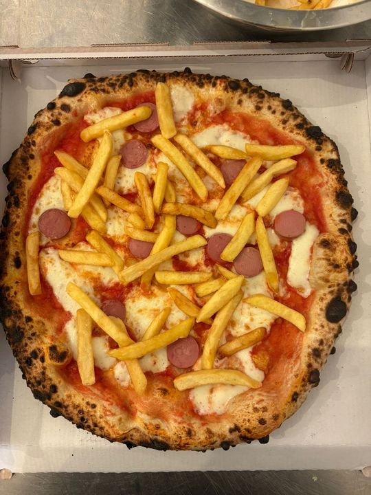 Pizza in scatola, condita con patatine fritte e salsicce a fette, con una crosta bruciacchiata.