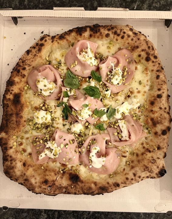 Pizza su un piatto bianco, con prosciutto, funghi e salsa di pomodoro, posta su un piano di lavoro in granito.