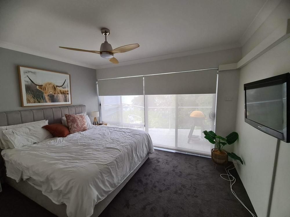 A Bedroom with A Bed, Ceiling Fan, and Sliding Glass Doors with Blinds — Barry's Affordable Blinds in Taylors Beach, NSW