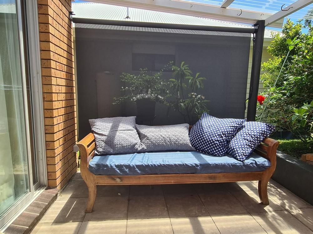 A Wooden Couch Is Sitting on A Patio With An Awning — Barry's Affordable Blinds in Taylors Beach, NSW
