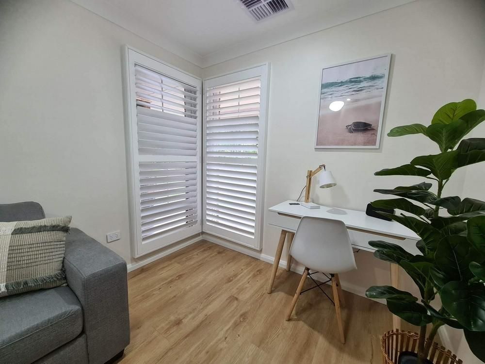 A Living Room with A Desk, Chair and Shutters — Barry's Affordable Blinds in Taylors Beach, NSW