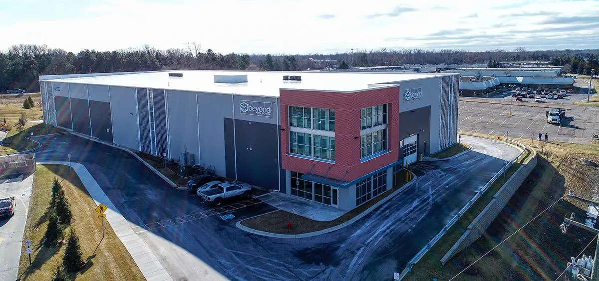 A large gray industrial building with a red accent, set in an outdoor area on a sunny day.