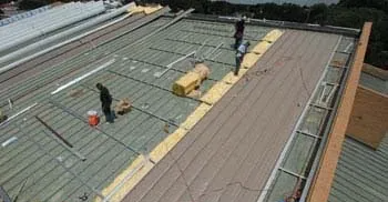 Workers installing insulation on a metal roof, tools and materials present.