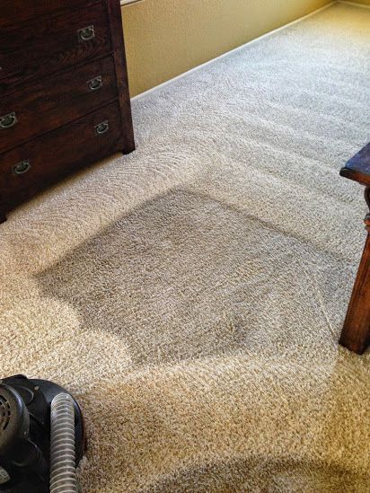A vacuum cleaner is cleaning a carpet in a bedroom.