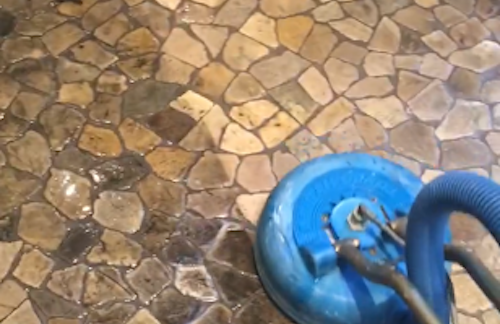 A blue vacuum cleaner is cleaning a stone floor.