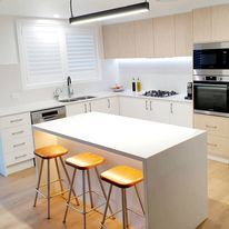 Indoor White Kitchen With Stools Side View — DMB Kitchens in Port Macquarie, NSW