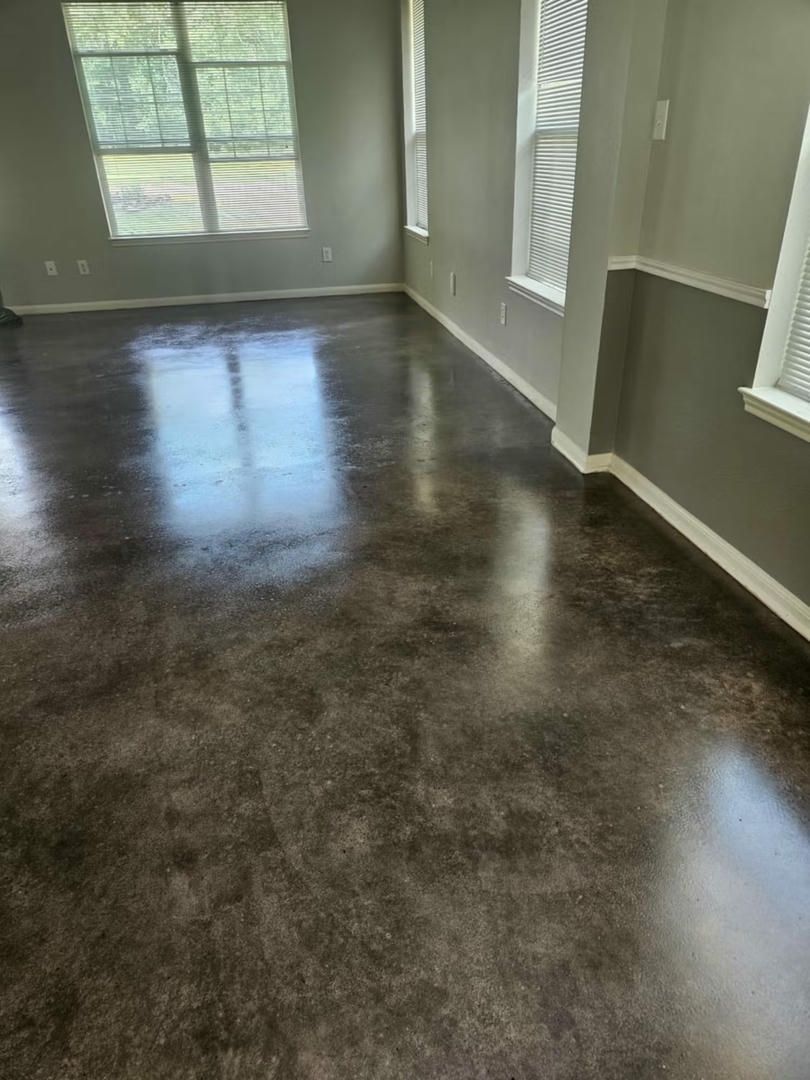 Dark, glossy, stained concrete floor in a room with gray walls and white trim; windows on the wall.