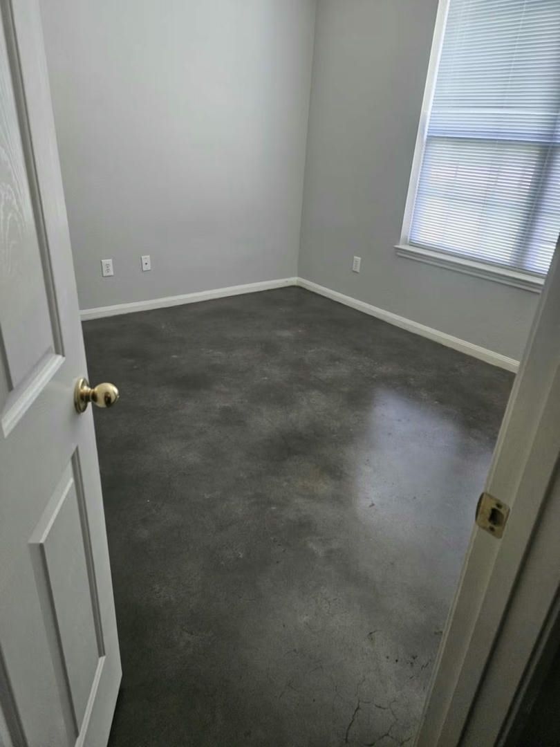 Empty room with gray walls and a concrete floor, window with blinds.