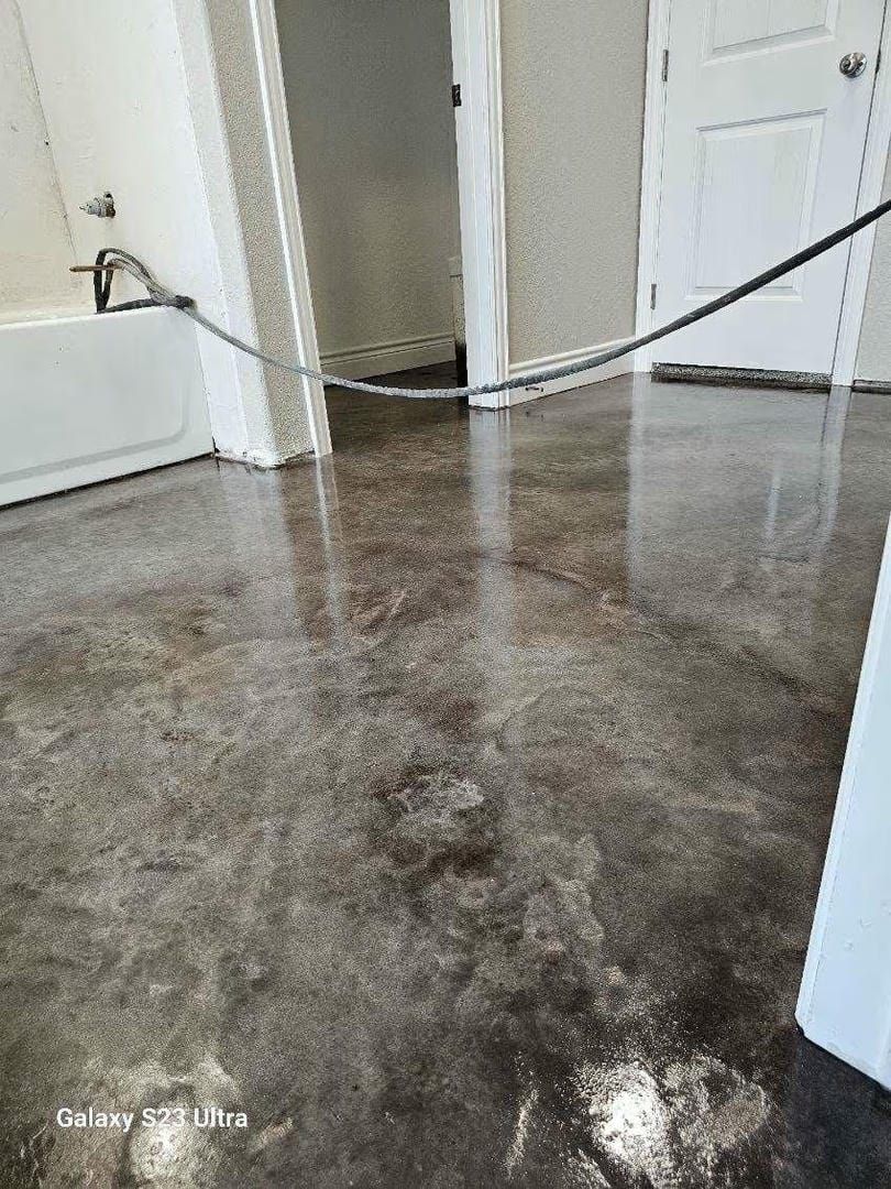 Polished concrete bathroom floor reflects light; a tub and two doorways are visible.