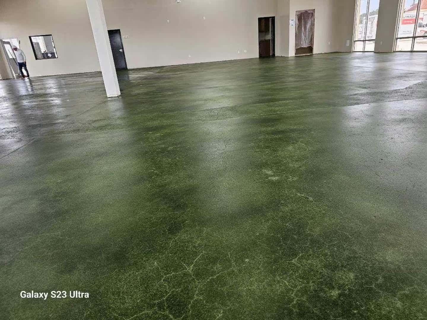 Green-toned concrete floor in a large empty room with white pillars and dark doorways.