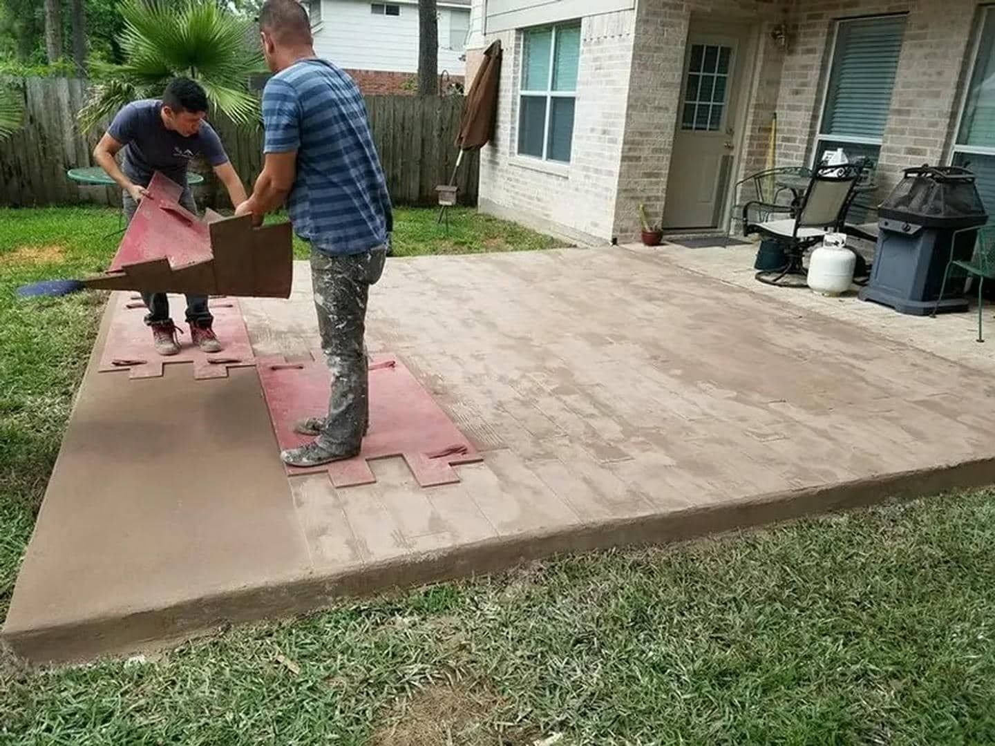 Two people installing interlocking tiles on a concrete patio.
