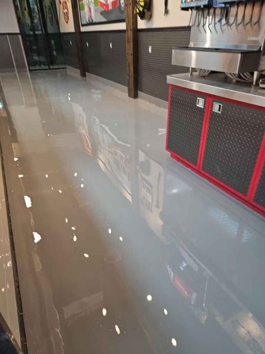 Interior of a metal building with a stained concrete floor. Large windows and door let in light.