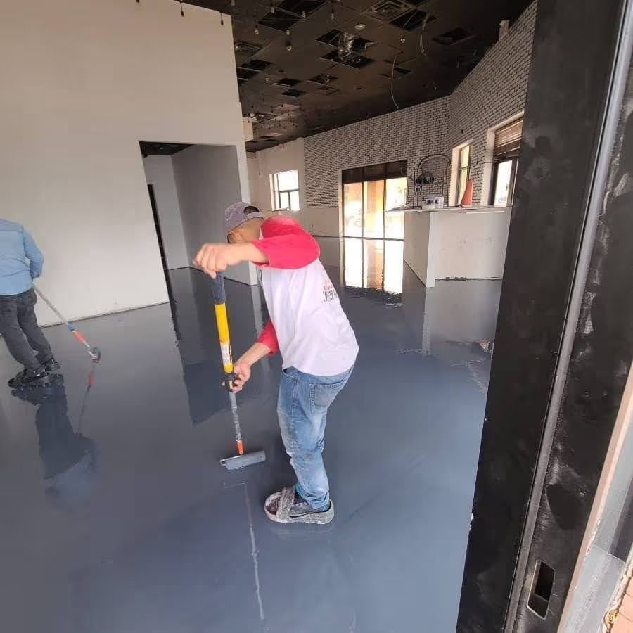 Two people painting a gray epoxy floor inside a commercial building.