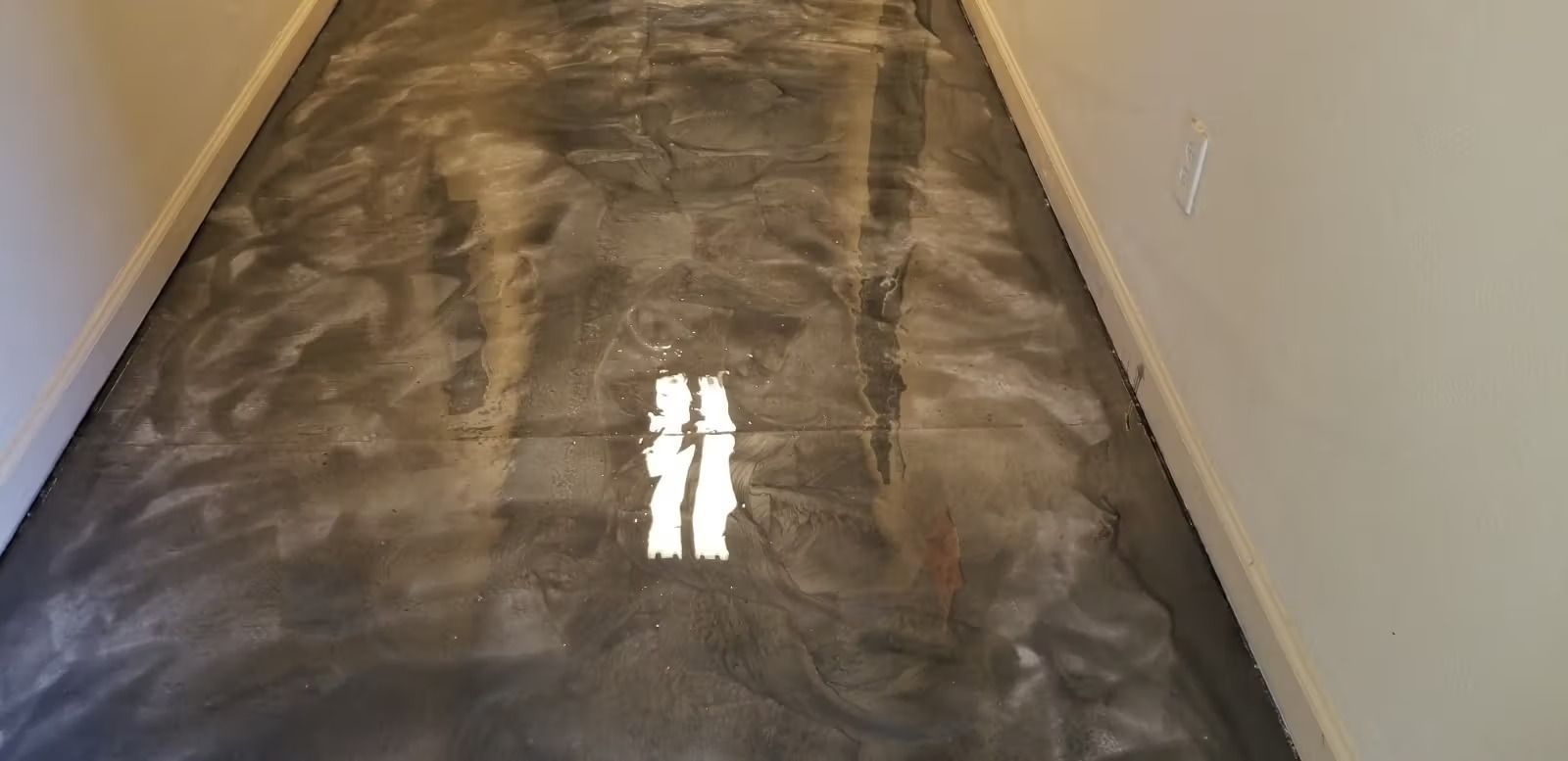 Two people apply dark gray epoxy floor coating to an interior space.