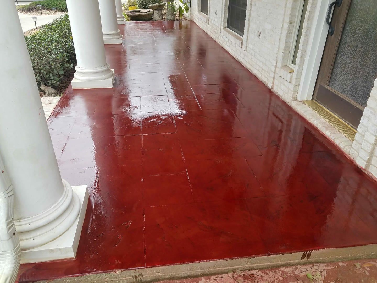 Red-painted concrete porch with white columns. The surface is shiny and reflects the surrounding elements.