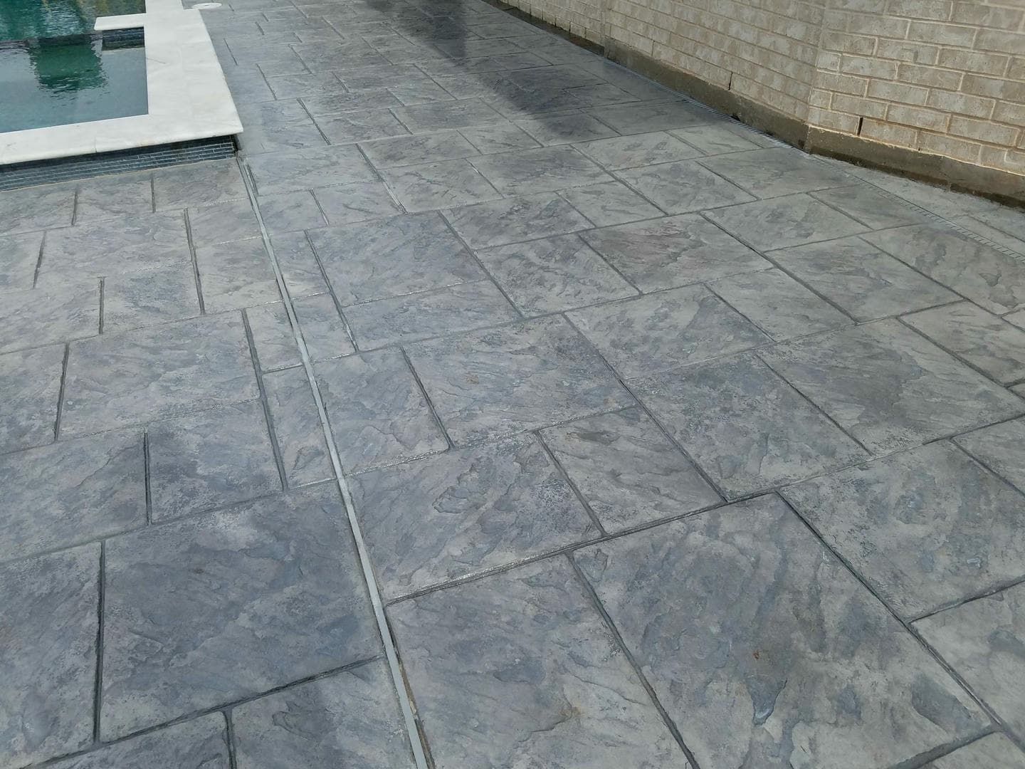 Gray stamped concrete patio with geometric pattern next to a swimming pool.