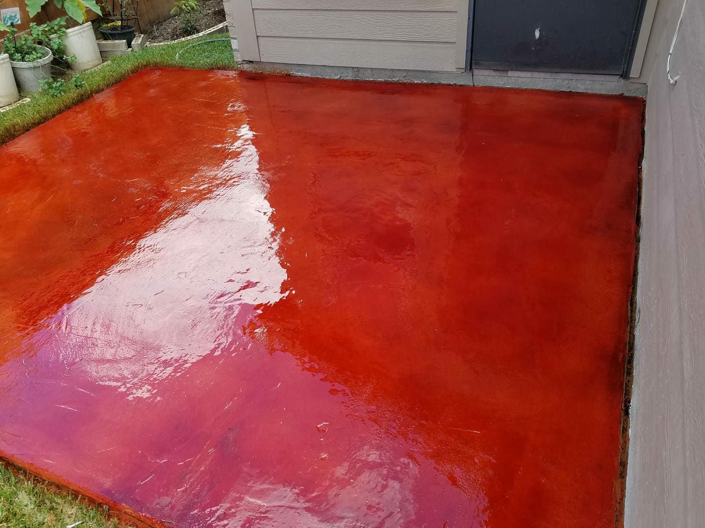 Red-stained concrete patio reflecting sunlight near a building.