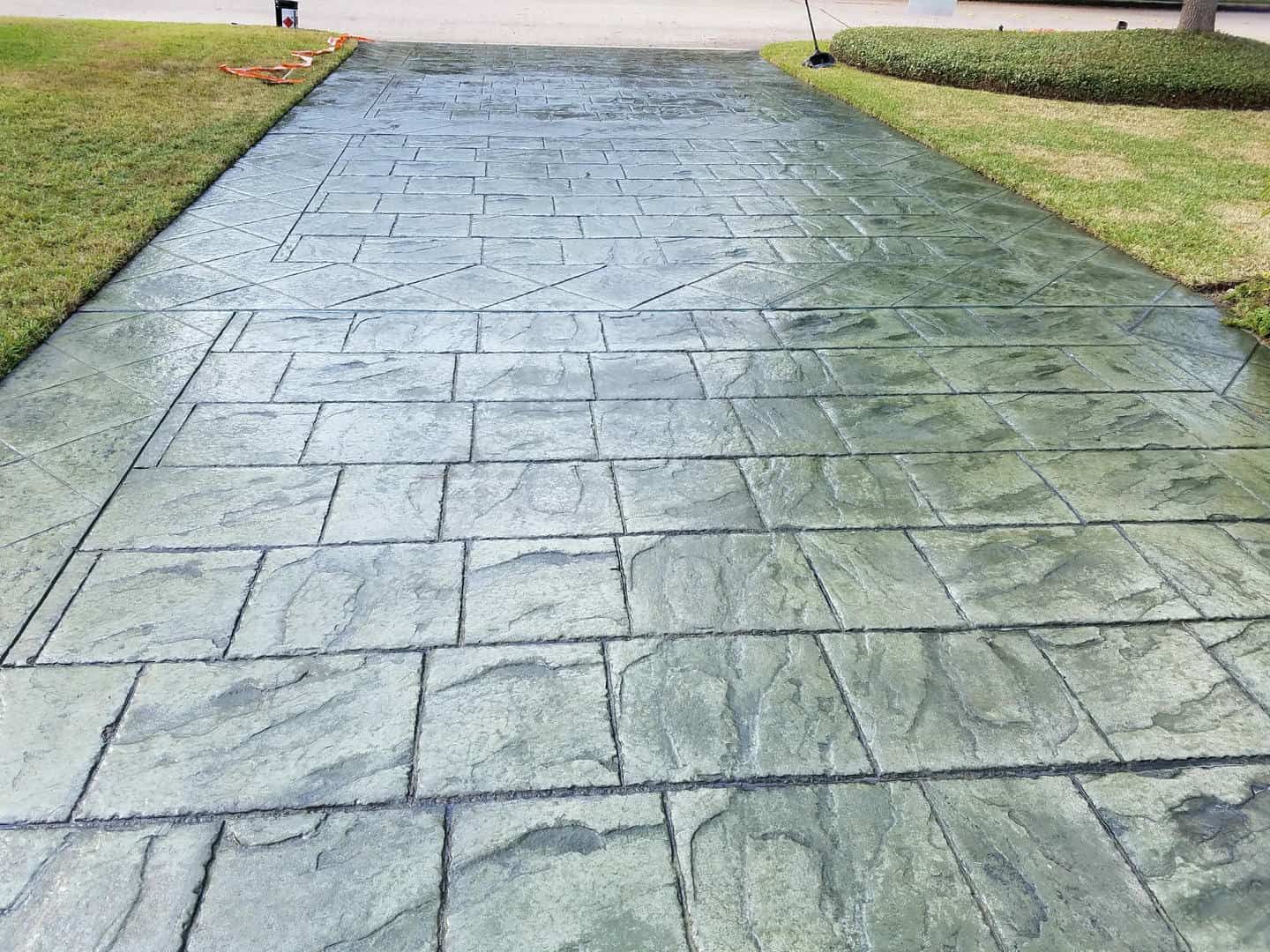 Gray stamped concrete driveway with a stone-like pattern, flanked by green grass.