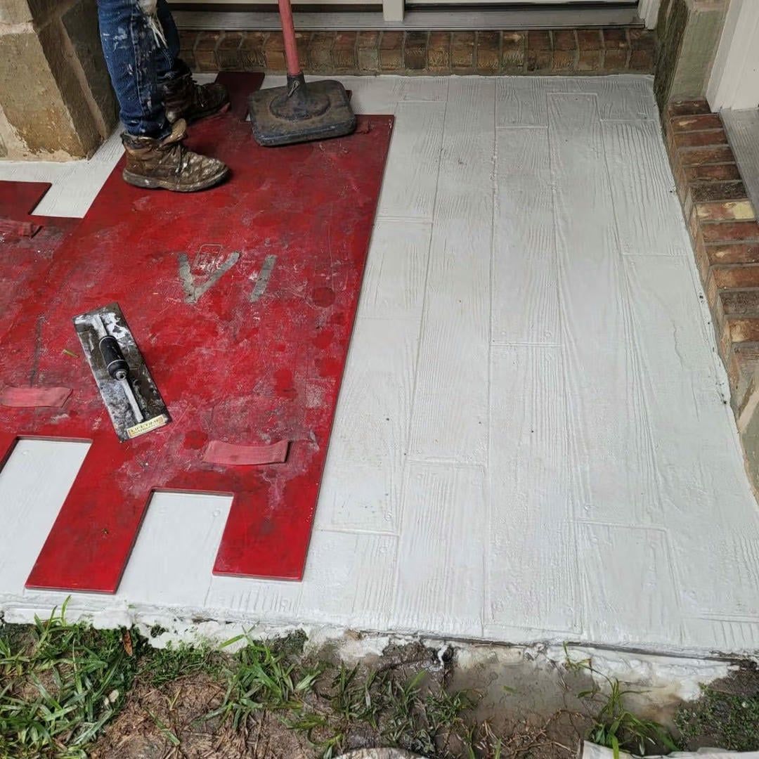 A person stamping wood-grain pattern into concrete porch. Red mat and trowel present.