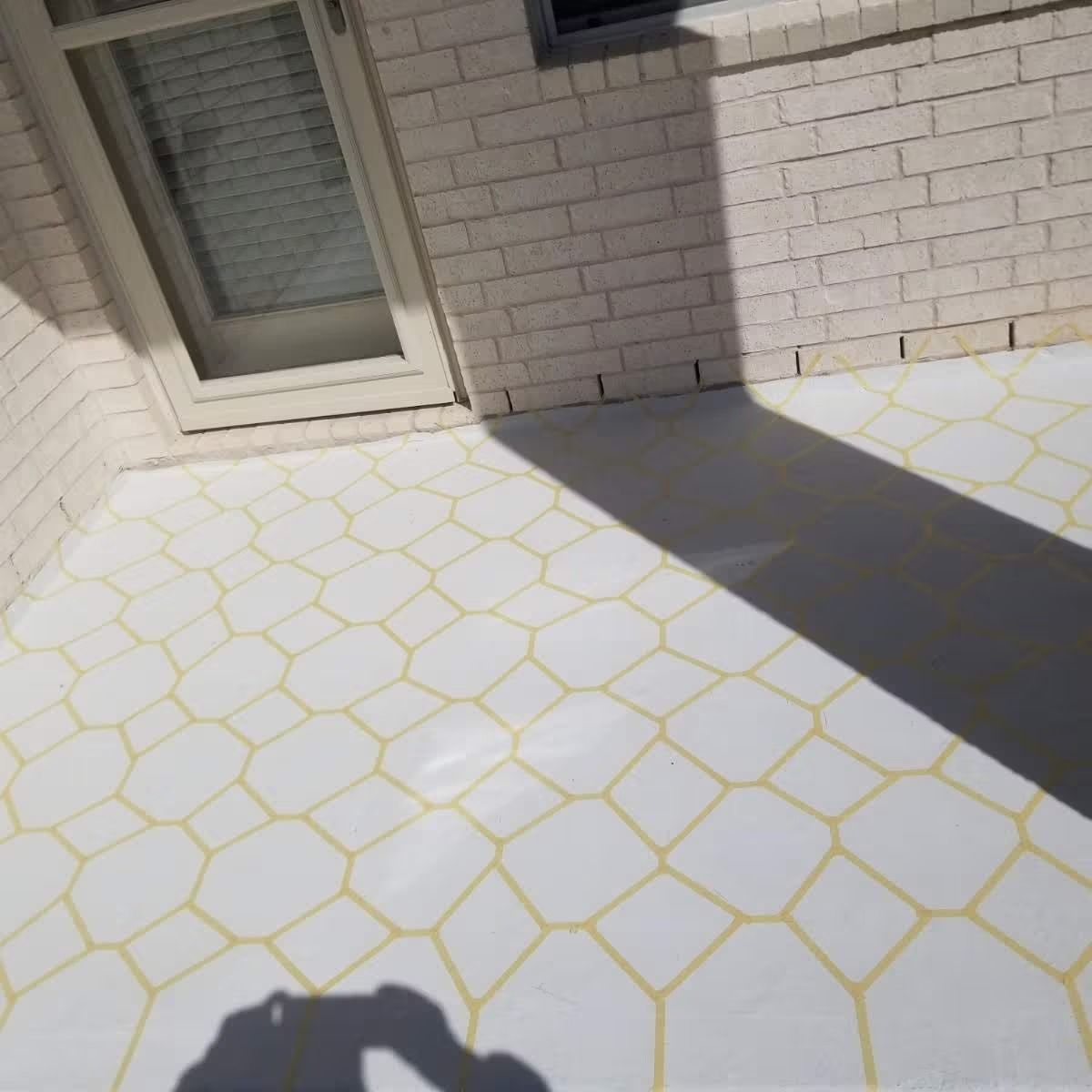 White and yellow honeycomb-patterned concrete patio next to a brick wall and door.