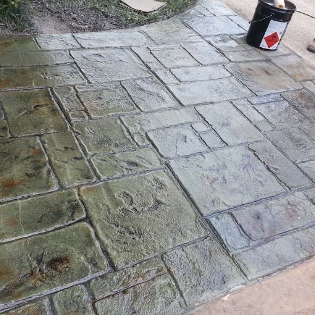 Stamped concrete patio with a flagstone pattern, various shades of gray and green. A bucket sits on the concrete.