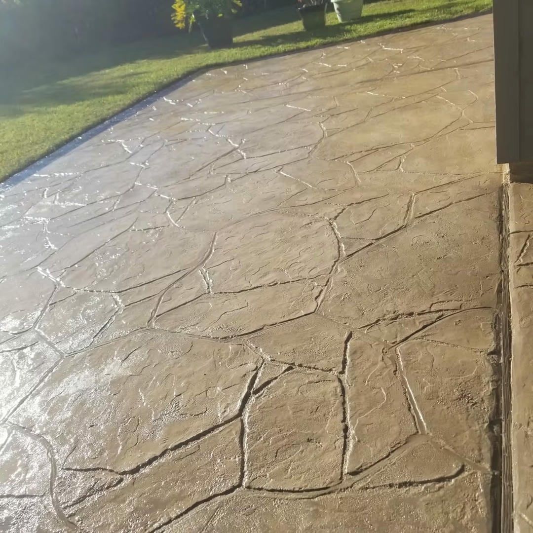 Textured concrete patio with a flagstone pattern, bordering grass and a building.