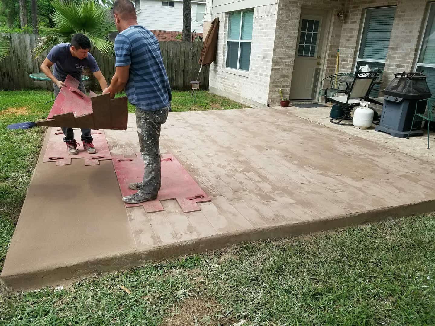 Two people installing interlocking floor tiles on a concrete patio.