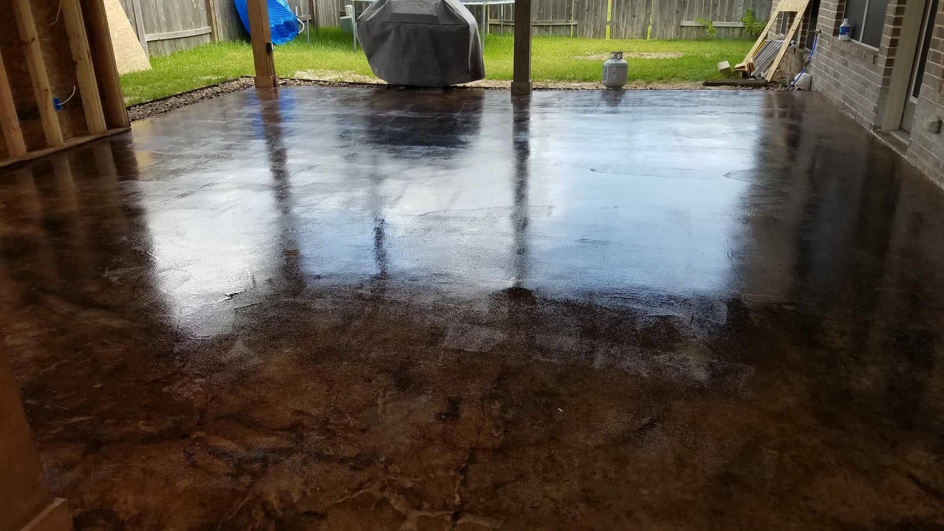 Brown, glossy concrete patio reflecting the sky. Wooden framing on the left.