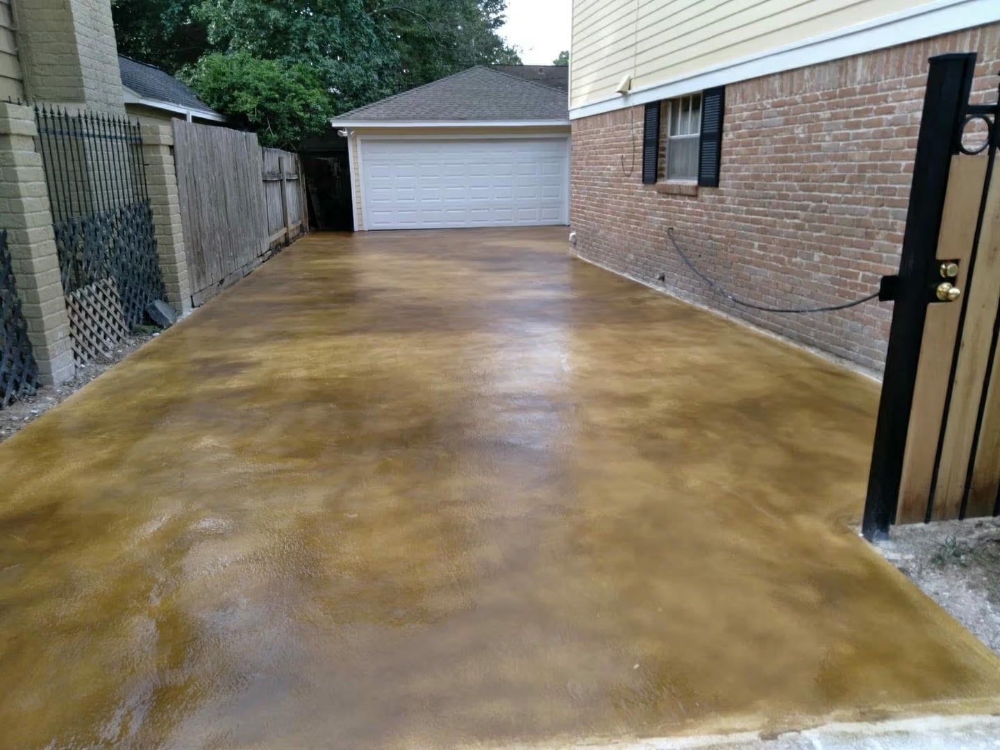 Brown-stained concrete driveway leading to a garage.  A brick wall and fence flank the sides.