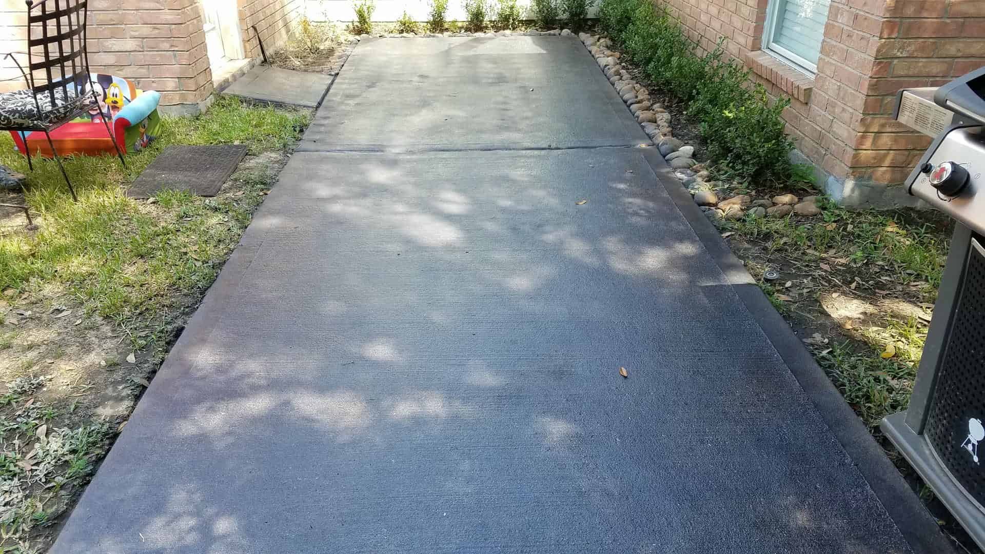 Black rubber walkway in a yard, bordered by grass and plants, with a grill visible.