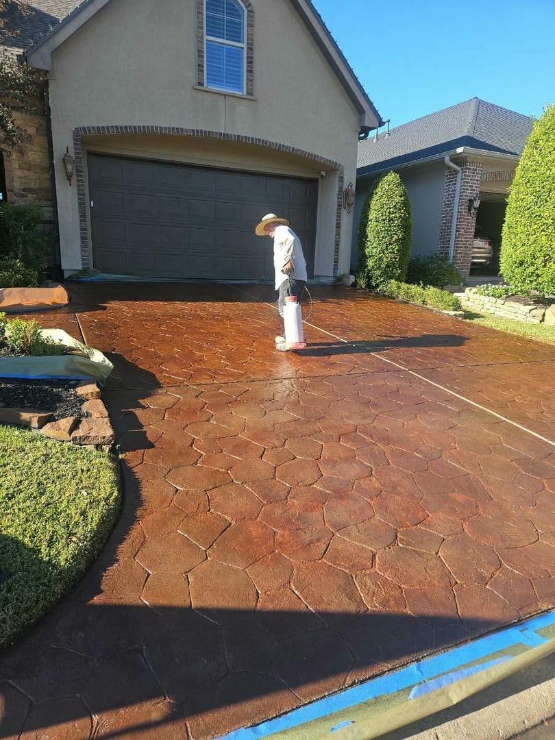 Person standing on a freshly stained brown driveway in front of a house with a garage.