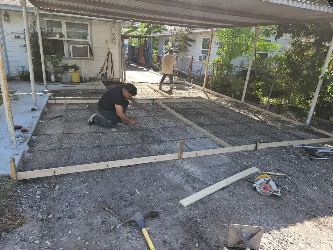 Man kneeling, working on a concrete slab foundation under a covered patio.